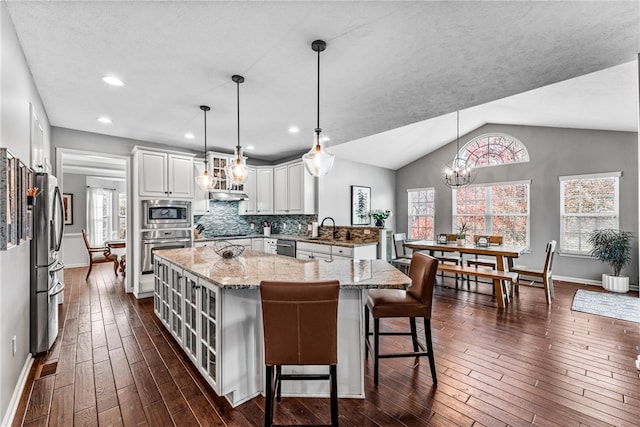 kitchen featuring dark wood-type flooring, vaulted ceiling, hanging light fixtures, and appliances with stainless steel finishes