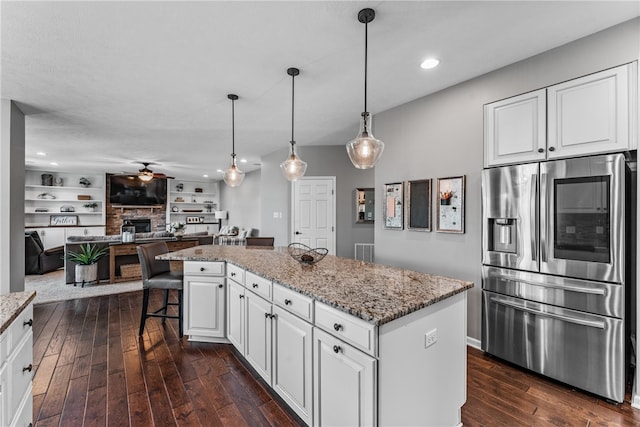 kitchen with light stone counters, stainless steel fridge, dark hardwood / wood-style flooring, white cabinets, and a center island