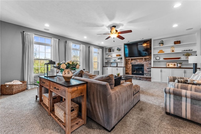 carpeted living room featuring a stone fireplace, a textured ceiling, ceiling fan, and built in shelves