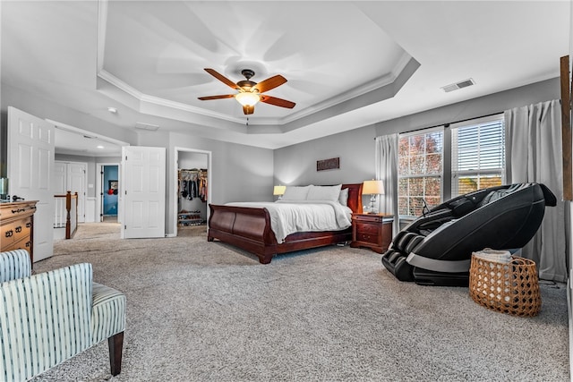 carpeted bedroom featuring ornamental molding, ceiling fan, a tray ceiling, a walk in closet, and a closet