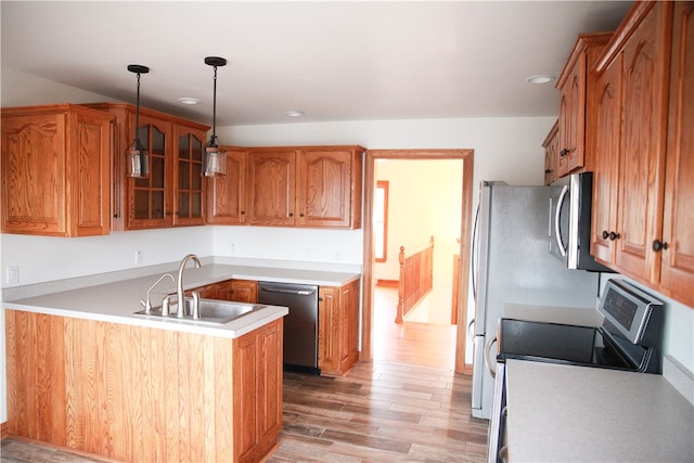 kitchen with stainless steel appliances, pendant lighting, sink, kitchen peninsula, and light hardwood / wood-style flooring