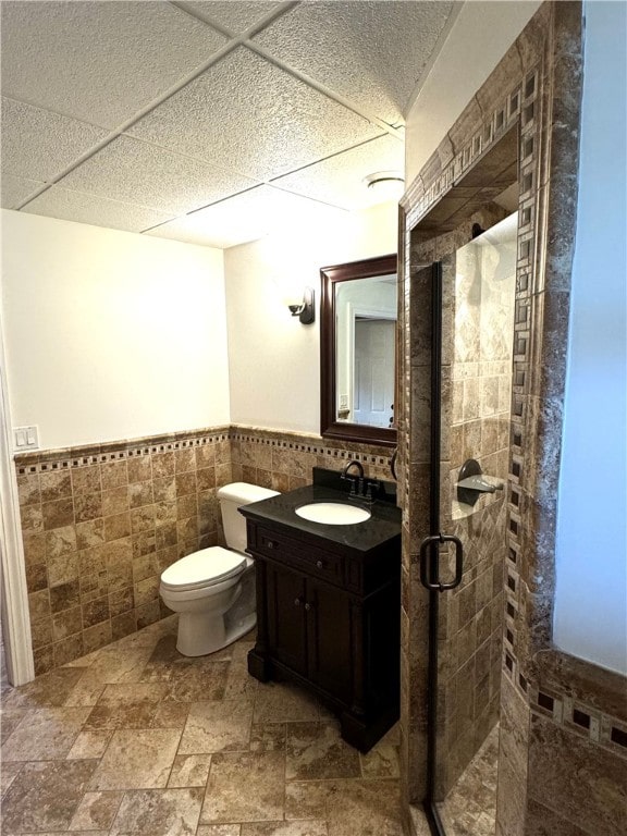 bathroom featuring tile walls, vanity, toilet, and a shower with shower door