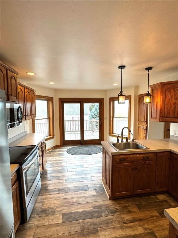 kitchen with appliances with stainless steel finishes, dark hardwood / wood-style floors, pendant lighting, sink, and kitchen peninsula