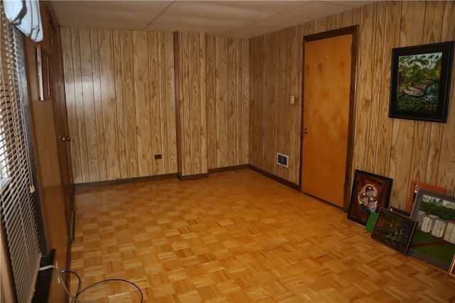 empty room with wood walls, a paneled ceiling, and light parquet floors