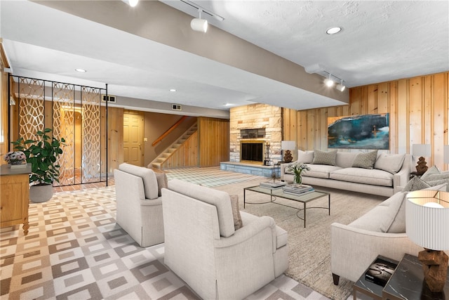 carpeted living room with a stone fireplace, rail lighting, and wooden walls