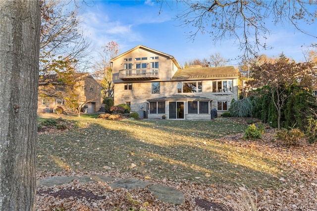 rear view of property with central air condition unit, a sunroom, a lawn, and a balcony