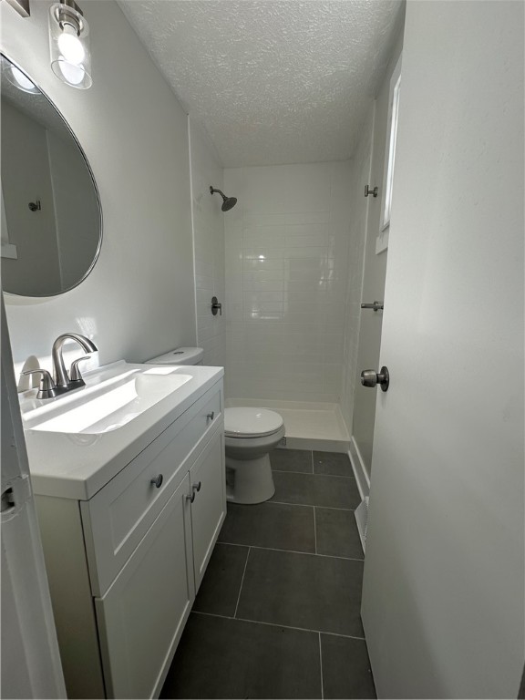 bathroom featuring a tile shower, vanity, a textured ceiling, tile patterned flooring, and toilet