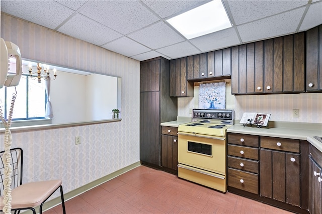 kitchen featuring dark brown cabinets, stove, a chandelier, and a drop ceiling