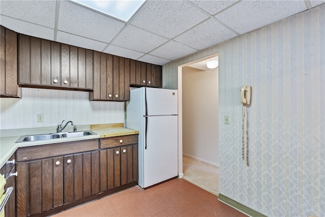 kitchen with a drop ceiling, sink, dark brown cabinets, and white refrigerator