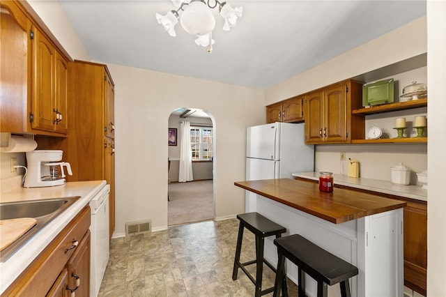 kitchen with a kitchen bar, light carpet, white appliances, sink, and butcher block countertops