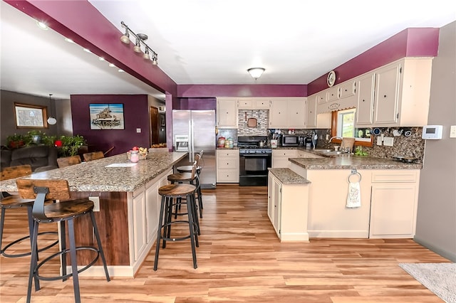 kitchen featuring stainless steel appliances, light hardwood / wood-style floors, kitchen peninsula, stone counters, and a kitchen breakfast bar