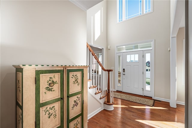 entrance foyer with a towering ceiling, hardwood / wood-style flooring, a healthy amount of sunlight, and crown molding