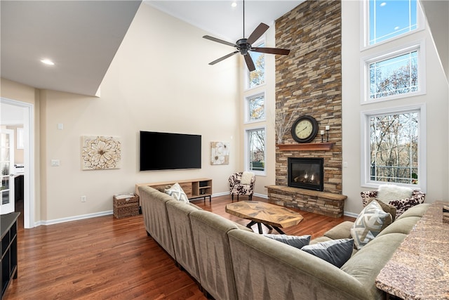 living room featuring a stone fireplace, dark hardwood / wood-style flooring, ceiling fan, and a towering ceiling