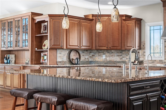 kitchen featuring dark stone counters, a kitchen breakfast bar, decorative light fixtures, hardwood / wood-style floors, and decorative backsplash