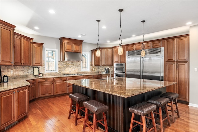 kitchen featuring a center island with sink, stainless steel appliances, pendant lighting, hardwood / wood-style floors, and a breakfast bar