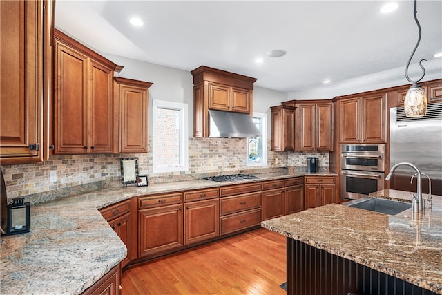 kitchen featuring stainless steel appliances, light hardwood / wood-style floors, sink, light stone countertops, and decorative light fixtures