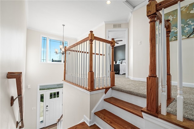 staircase featuring ceiling fan with notable chandelier and crown molding