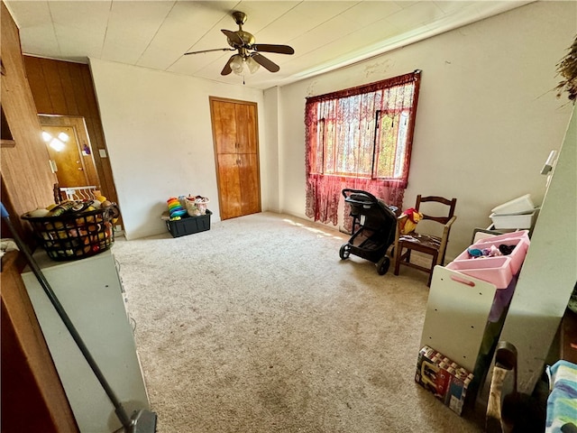 interior space with carpet, wooden walls, and ceiling fan