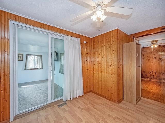 empty room with light wood-type flooring, wood walls, and ceiling fan