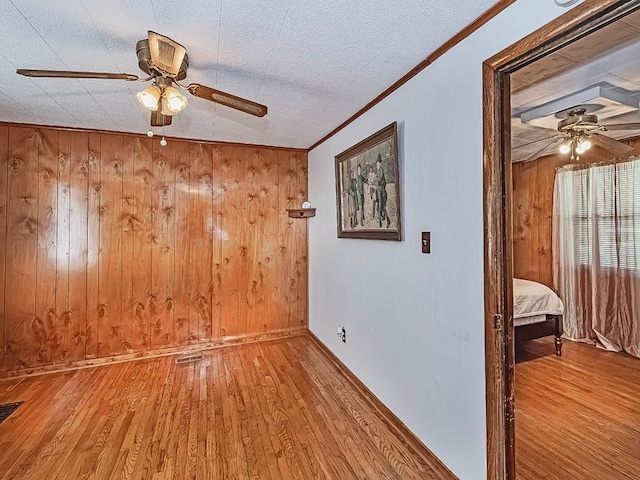 empty room with wood walls, a textured ceiling, ceiling fan, crown molding, and light wood-type flooring