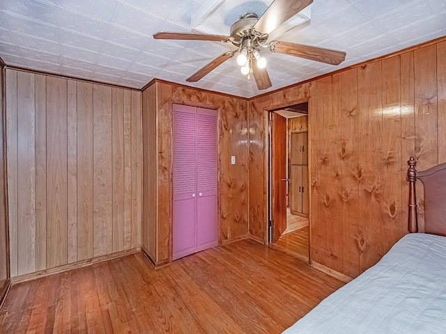 unfurnished bedroom featuring wood walls, ceiling fan, a closet, and light wood-type flooring