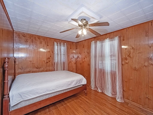 bedroom with multiple windows, light hardwood / wood-style flooring, wood walls, and ceiling fan