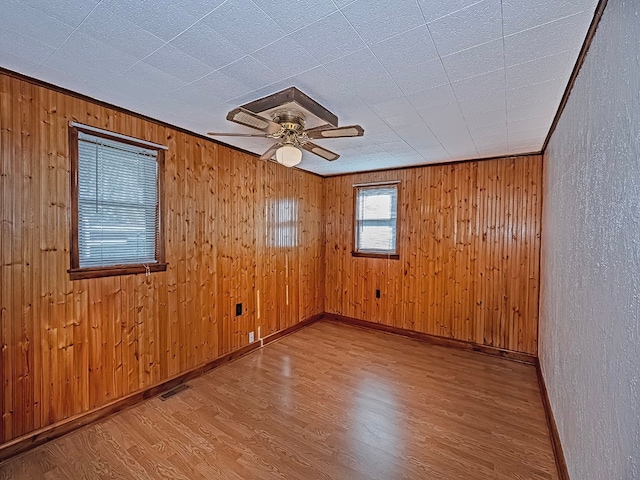 empty room with hardwood / wood-style floors, ceiling fan, wood walls, and ornamental molding