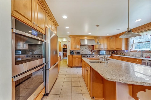 kitchen with sink, hanging light fixtures, wall chimney range hood, and appliances with stainless steel finishes