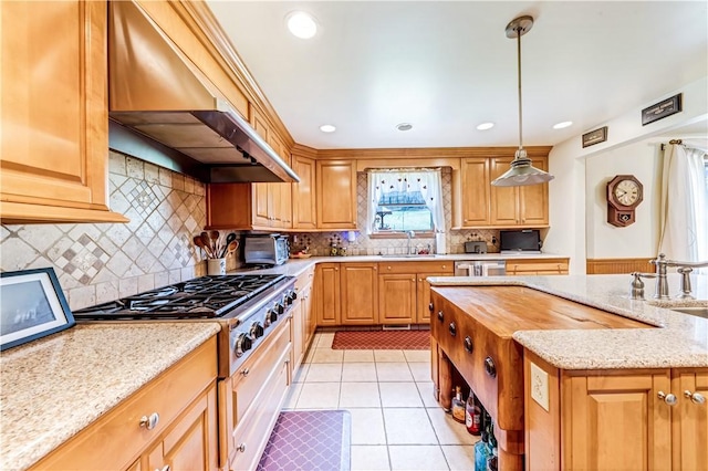 kitchen featuring light stone countertops, hanging light fixtures, wall chimney range hood, stainless steel gas stovetop, and light tile patterned floors