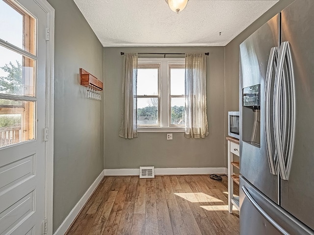 interior space featuring stainless steel refrigerator with ice dispenser, a textured ceiling, and light hardwood / wood-style flooring