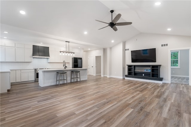 unfurnished living room with ceiling fan, sink, light wood-type flooring, and vaulted ceiling