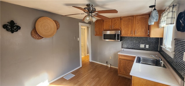 kitchen with backsplash, light wood-type flooring, pendant lighting, sink, and ceiling fan