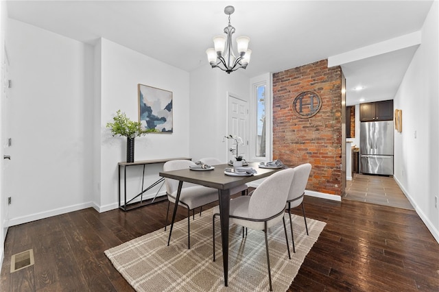 dining space with dark hardwood / wood-style flooring, a chandelier, and brick wall