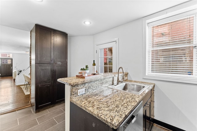 kitchen with kitchen peninsula, sink, stainless steel dishwasher, light stone countertops, and light wood-type flooring