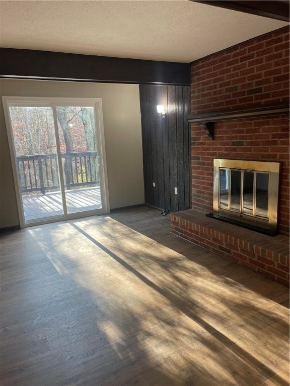 unfurnished living room with dark wood-type flooring, a textured ceiling, and a brick fireplace