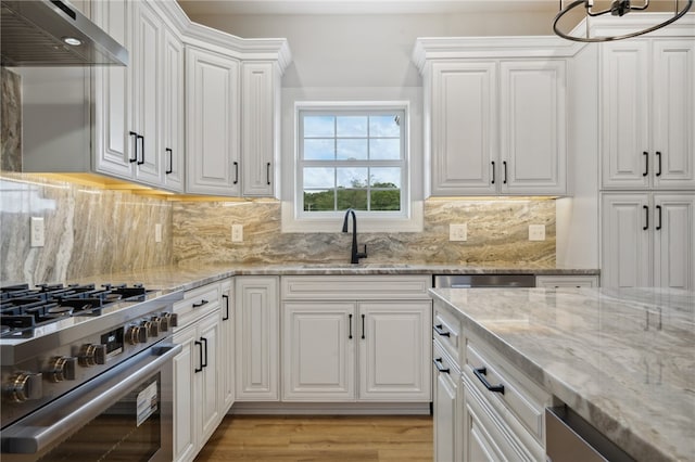 kitchen with light hardwood / wood-style floors, sink, appliances with stainless steel finishes, white cabinets, and wall chimney range hood