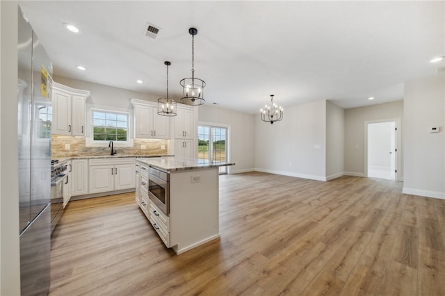 kitchen featuring white cabinetry, decorative light fixtures, light stone countertops, light hardwood / wood-style floors, and a center island