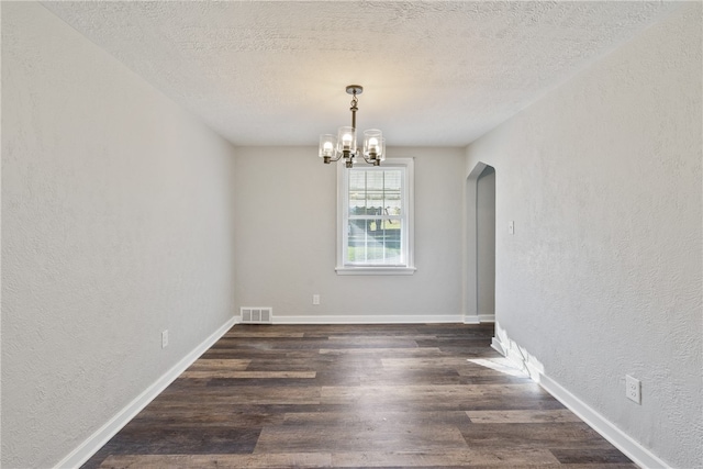 spare room featuring dark wood-type flooring, a textured ceiling, and a notable chandelier