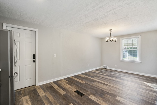 unfurnished room featuring a chandelier, a textured ceiling, and dark hardwood / wood-style flooring