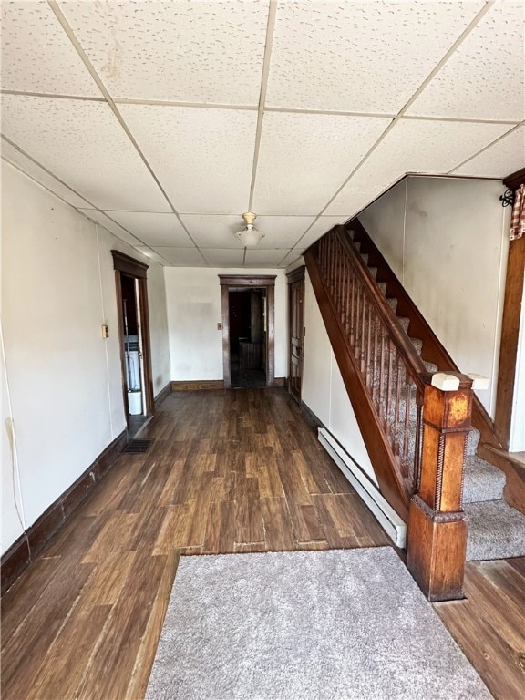 interior space with a baseboard heating unit, dark hardwood / wood-style floors, and a drop ceiling