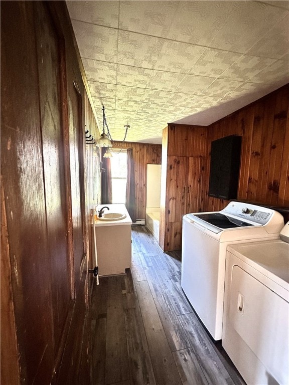 washroom featuring dark wood-type flooring, wooden walls, sink, and washer and clothes dryer