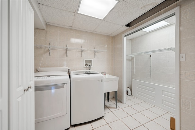 laundry room featuring washing machine and clothes dryer, light tile patterned floors, and tile walls