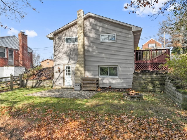 back of property featuring a wooden deck, a fire pit, a lawn, and a patio area