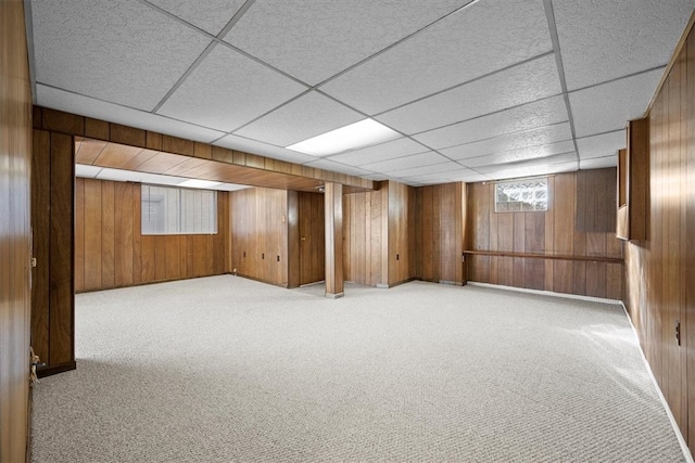 basement with wood walls, a paneled ceiling, and light colored carpet