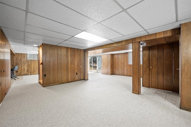 basement featuring wooden walls, a drop ceiling, and light colored carpet