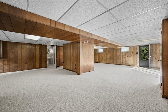 basement with wood walls, a drop ceiling, and carpet flooring