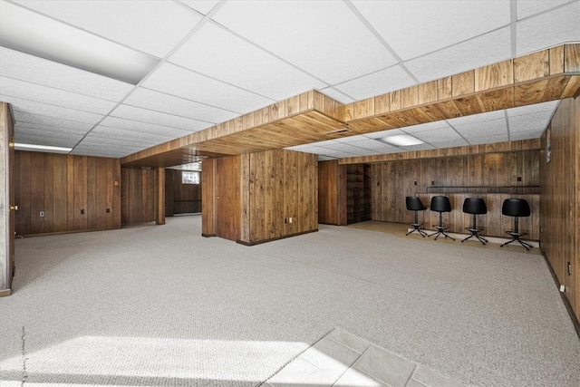 basement featuring a paneled ceiling, wooden walls, and light carpet