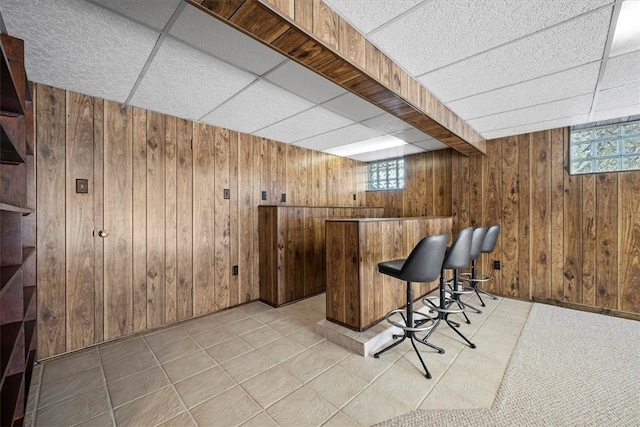 bar with a drop ceiling, wood walls, and light tile patterned floors