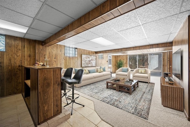 living room with a drop ceiling, wood walls, and light tile patterned floors