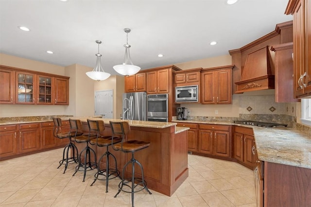 kitchen featuring appliances with stainless steel finishes, custom range hood, a breakfast bar area, an island with sink, and pendant lighting